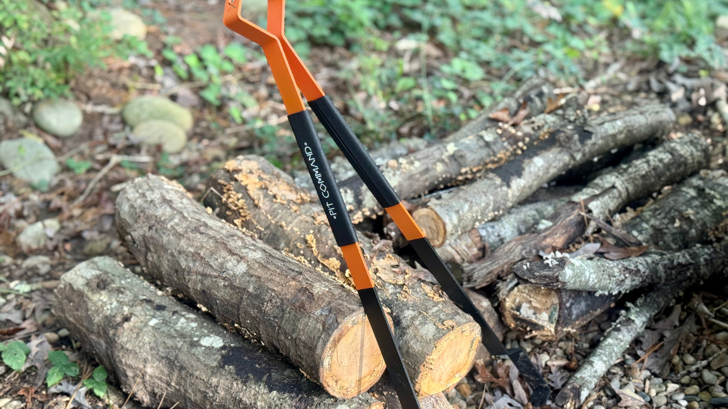 set of long black and orange stainless steel Pit Command Talons leaning against pile of chopped wood